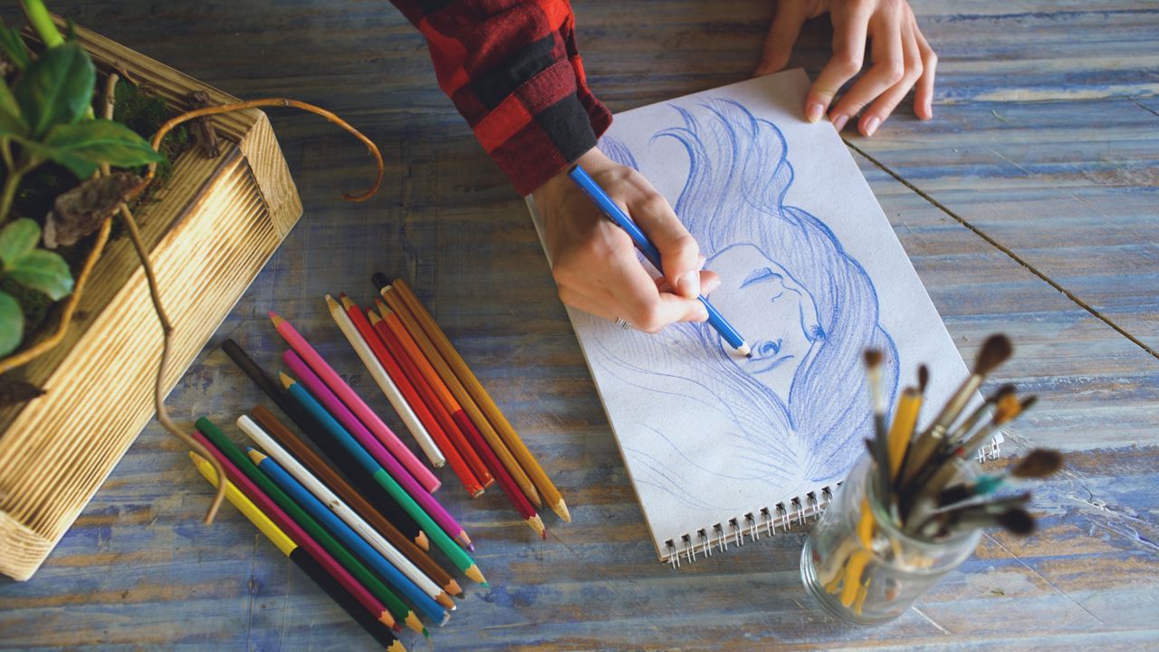 Crafting Captivating Headlines: Your awesome post title goes here Top view of a person drawing a portrait with color pencils on wooden table.