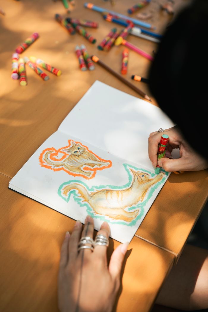 A person drawing vibrant animals with crayons in a sketchbook on a sunny day.