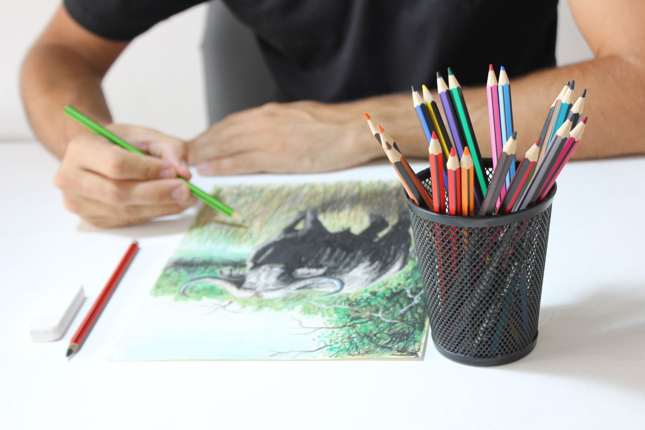 Close-up of an artist drawing with colored pencils, featuring detailed elephant artwork on paper.