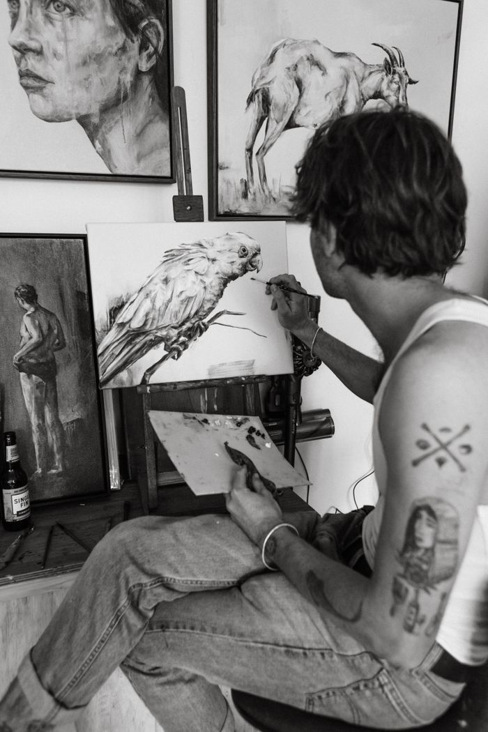 Mastering the First Impression: Your intriguing post title goes here Side view of black and white young tattooed male sitting on chair and drawing various pictures with paintbrush in creative studio