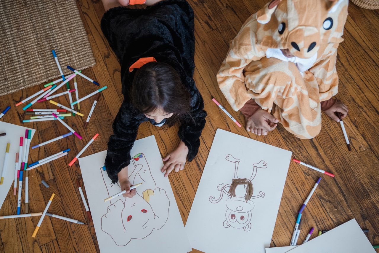 Offerings Two children in animal costumes coloring with markers on the wooden floor.